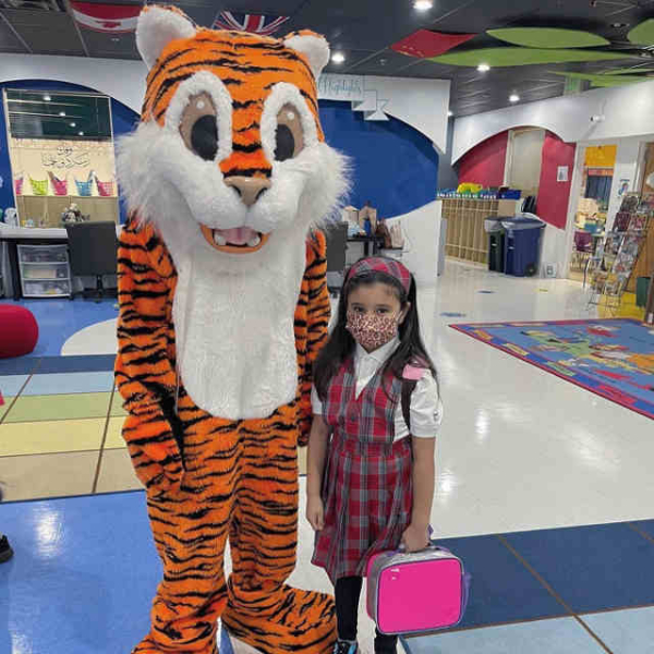 Tarbiyah Tiger Mascot standing next to girl in red and blue plaid jumper with white shirt